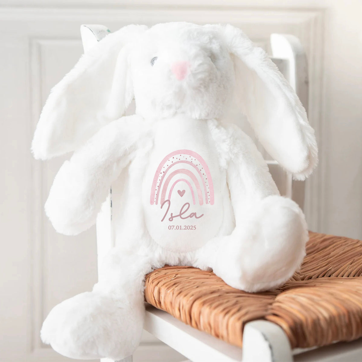 White soft bunny toy with personalised name and pink rainbow print on the front. A timeless keepsake by Ayla & Lara, perfect for baby gifts.