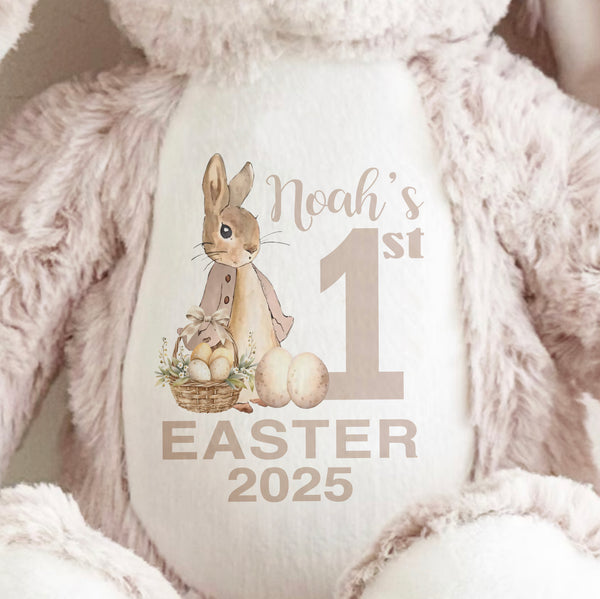 Close up of soft toy Beige Bunny with long ears sitting up with a Peter Rabbit Baby's First Easter 2025 printed on the front.